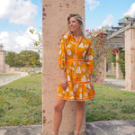 Woman in a yellow dress with a floral pattern standing outdoors near a stone column.